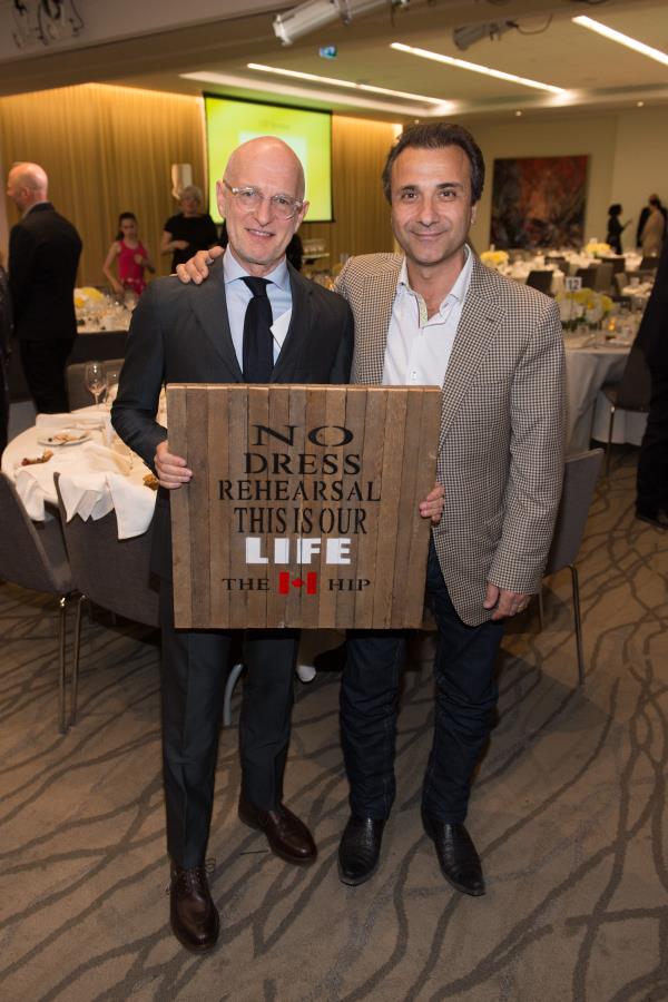 two men posing for camera at gala holding a wooden sign