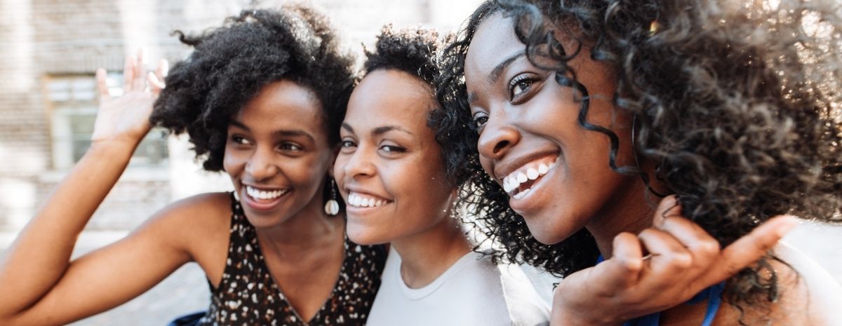 Three BIPOC women hugging and smiling