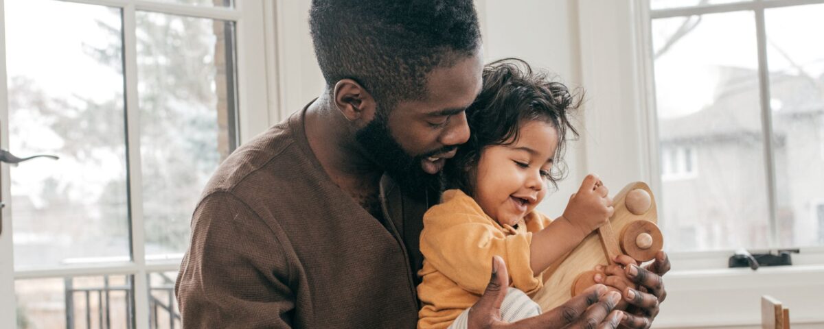 African American mindful father holding an infant while playing with a toy