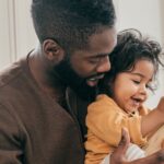 African American mindful father holding an infant while playing with a toy