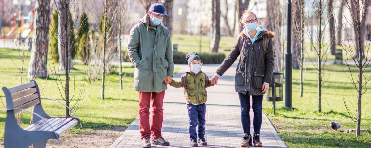 Mother and father holding their child's hand in the park while wearing face masks