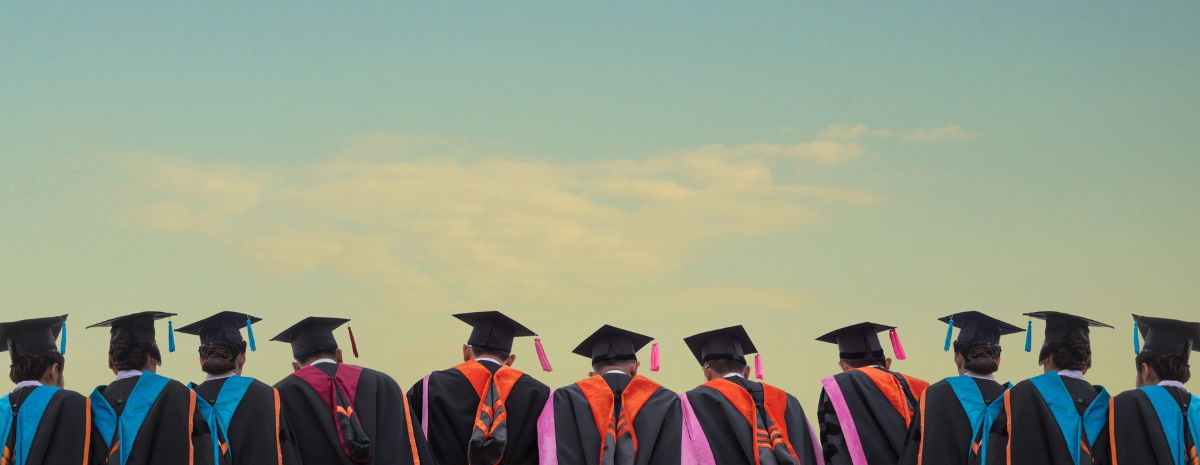 Post secondary school graduates facing forward in gown and cap
