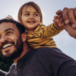 Happy father holding toddler on his shoulders with arms stretched out