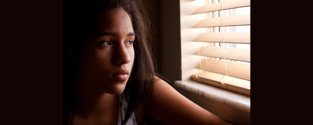 sad girl in a dark room looking out a window