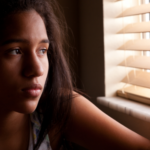 sad girl in a dark room looking out a window
